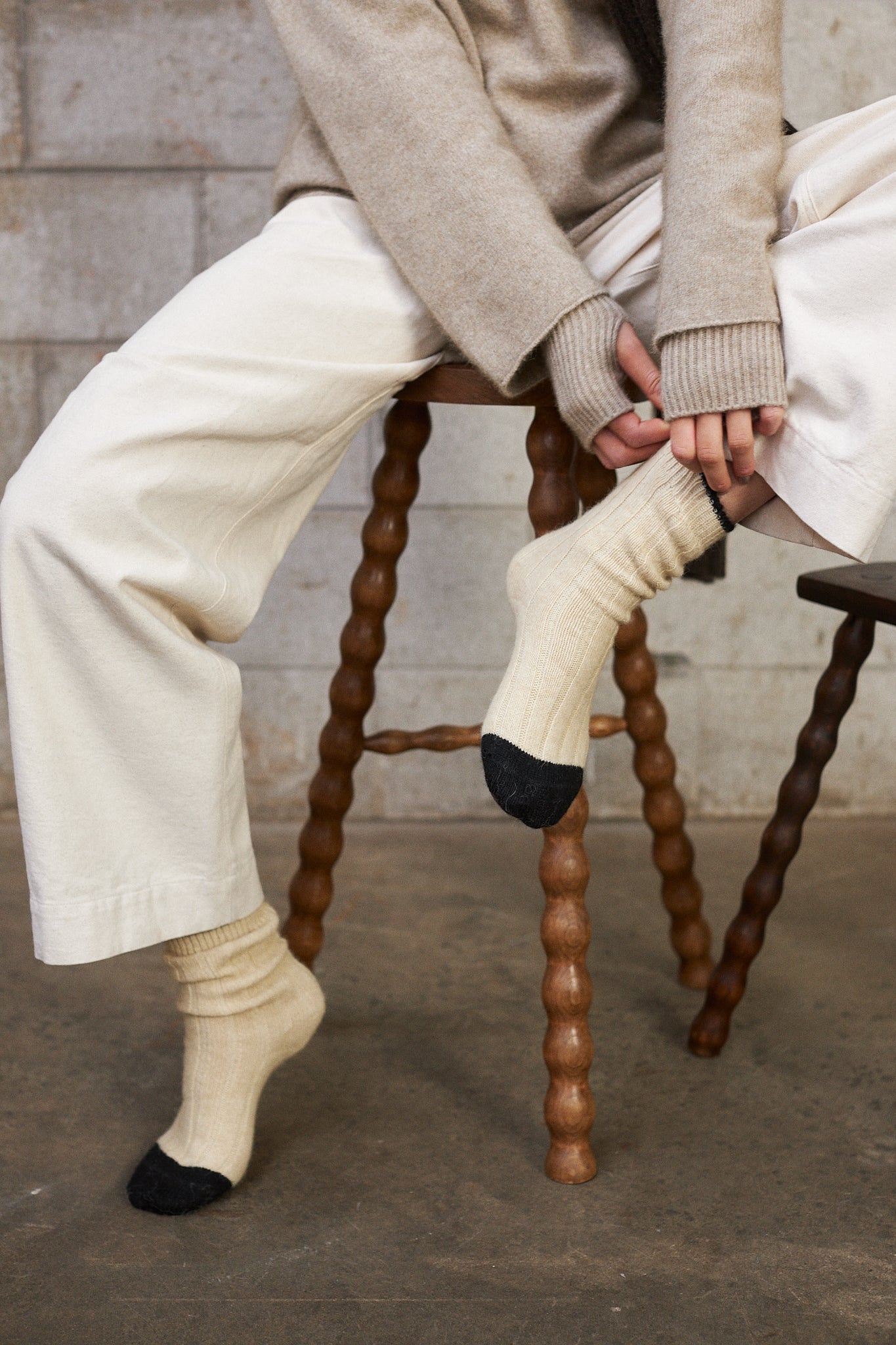 One person sitting on a wooden stool wearing beige pants and socks with black toes.
